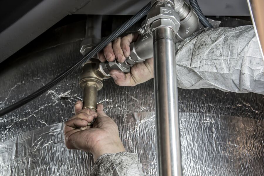 Hands tightening a fitting on a metal water pipe